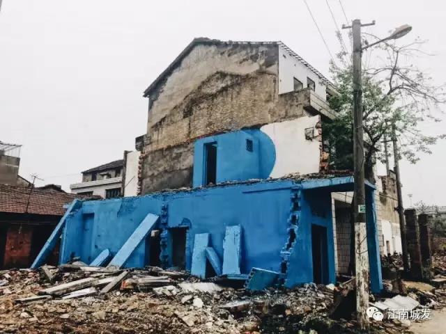 △ 這棟建筑是臨江最近的半拆遷建筑物的遺留，沅江和堤壩成為了展覽的天然背景。創(chuàng)作團(tuán)隊(duì)對這棟建筑進(jìn)行了半涂裝，將符號性的沅水曲線與拆遷進(jìn)行中的建筑立面進(jìn)行意義的疊造，它們共同觸發(fā)了場所空間多元語境的生成，把拆遷這種暫時(shí)破壞性、干擾性的介入行動(dòng)與沅水右岸發(fā)展的未來性、美好性緊密融合。